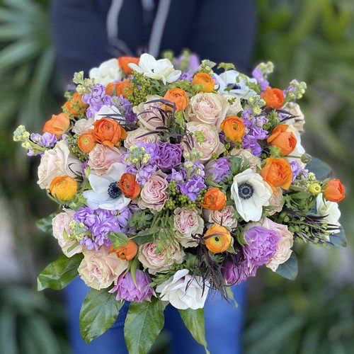 Hand-tied bouquet of orange ranunculus, lavender stock, and white anemones ready for delivery, high-end flower delivery Raleigh